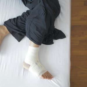 Top view of a bandaged foot resting on a bed, depicting injury and recovery.