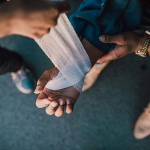 A detail shot showing hands applying a bandage to an injured wrist outdoors.